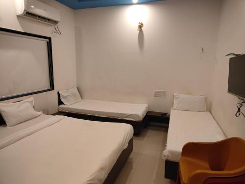 a room with two beds and a chair and a tv at S Sai Inn in Shirdi