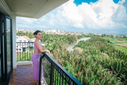 a woman standing on a balcony looking out over a river at Shining Riverside Hoi An Boutique & Spa in Hoi An