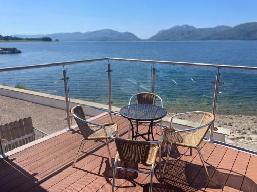 a table and chairs on a deck with a view of the water at Beach Houses with Hot Tubs in Glencoe