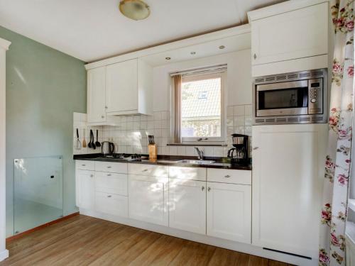 een witte keuken met witte kasten en een magnetron bij Holiday Home Villa Favorita by Interhome in Zonnemaire