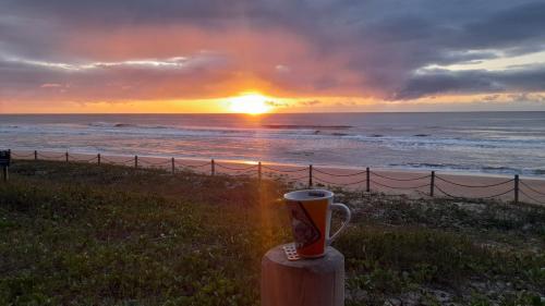 a cup of coffee sitting on a post near the ocean at Villa Tartarugas 2 - Casa Luxo e Conforto - 50m da Praia de Guriri in São Mateus