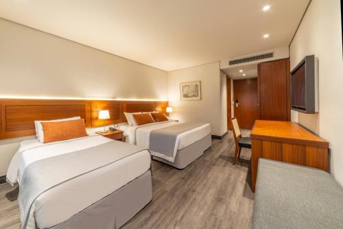 a hotel room with two beds and a desk at Laghetto Stilo São Paulo in Sao Paulo