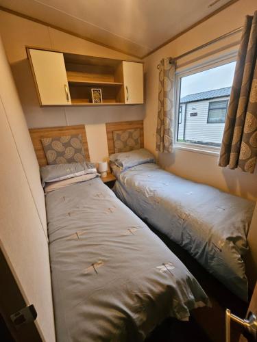 two beds in a small room with a window at KMH Caravans at Flamingo Land in Kirby Misperton