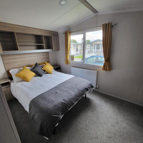a bedroom with a bed with yellow pillows and a window at KMH Caravans at Flamingo Land in Kirby Misperton