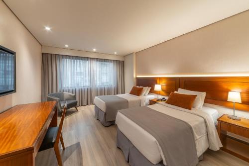 a hotel room with two beds and a desk at Laghetto Stilo São Paulo in Sao Paulo