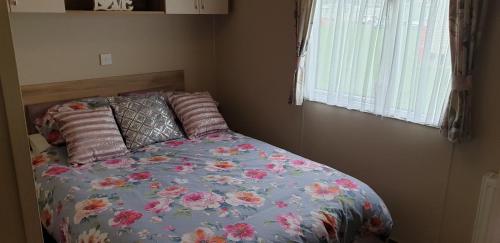 a bedroom with a bed with a floral comforter and a window at KMH Caravans at Flamingo Land in Kirby Misperton