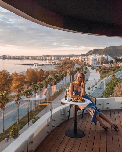 a woman sitting at a table on the balcony of a building at Yacht Hotel in Vlorë