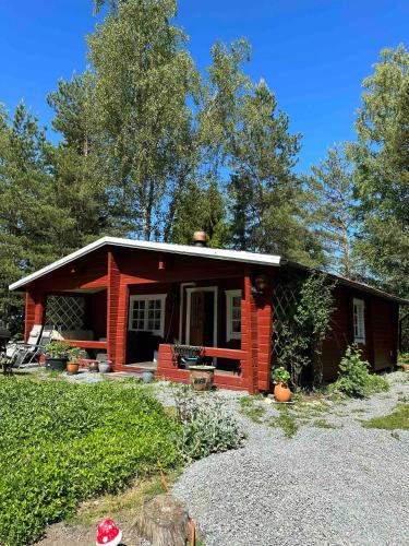 una pequeña casa roja con porche y árboles en A cosy cottage in Norrtälje en Norrtälje