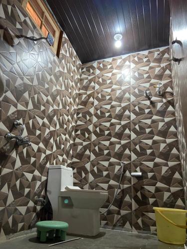 a bathroom with a toilet and a tiled wall at OTW Guest House & Mountain Cafe in Kasol