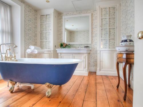 La salle de bains est pourvue d'une grande baignoire bleue et de parquet. dans l'établissement The Townhouse At Green Edge, à Beaumaris