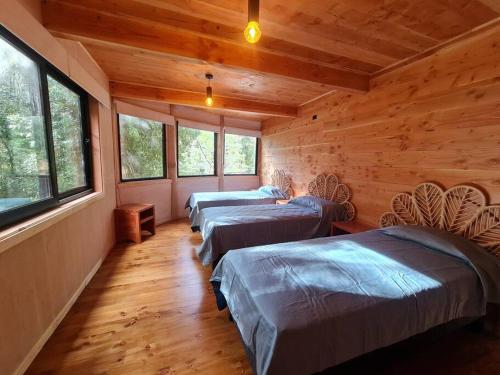 drie bedden in een kamer met houten wanden en ramen bij Mágica Casa Enclavada en el Corazón del Bosque in Huilo Huilo