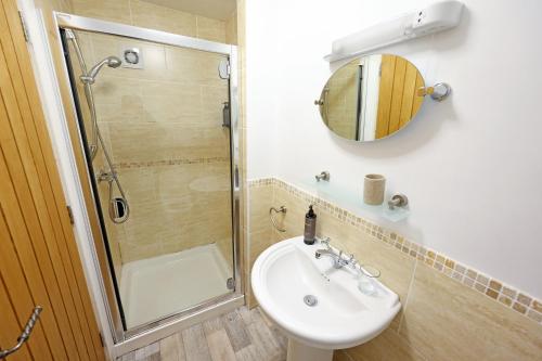 ein Bad mit einer Dusche, einem Waschbecken und einem Spiegel in der Unterkunft Sixty Six in Glenoe