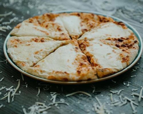 a cheese pizza on a pan on a table at 7 Rooms Hotel in Tserovani