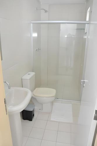 a white bathroom with a toilet and a glass shower at Pousada Aliança in Salvador