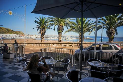 a woman sitting at a table with a view of a beach at Hotel Varandas do Atlântico by RIDAN Hotels in Praia da Vitória
