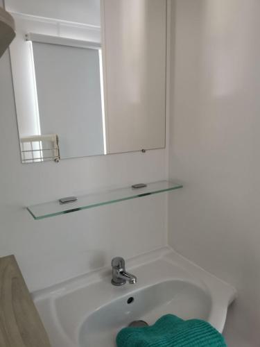 La salle de bains est pourvue d'un lavabo avec miroir et d'une serviette verte. dans l'établissement Mobil-home cosy 166, à Narbonne