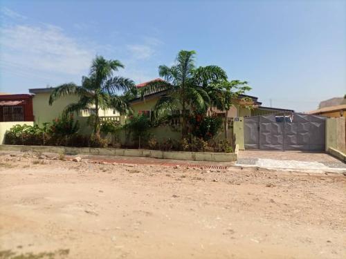 a house with palm trees in front of a dirt road at Emron Homelodge in Accra