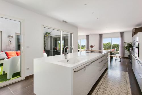 een witte keuken met een wastafel en een woonkamer bij Villa Le Golf St Thomas 19 pers in Béziers
