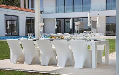una mesa de comedor blanca y sillas frente a una casa en Villa Vrsar Magnifique A Beautiful Contemporary 5 Bedroom Villa Sauna and Gym, en Vrsar