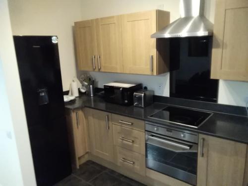 eine Küche mit Holzschränken und einem schwarzen Kühlschrank in der Unterkunft Savoy Court in Manchester