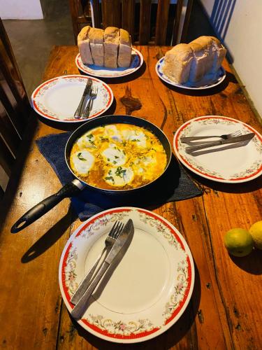 a wooden table with plates and utensils and bread at Tropicana Home Stay in Arugam Bay