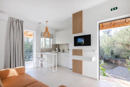 Peroulia Beach Houses في كوروني: مطبخ وغرفة معيشة مع دواليب بيضاء وتلفزيون