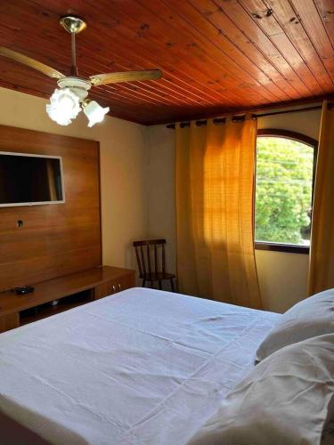 Un dormitorio con una cama con ventilador de techo y una ventana. en Casa Canto da Serra, en Búzios