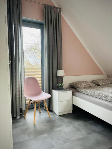 a bedroom with a bed and a pink chair at Coast House 25 -BALTIC GARDEN TRZĘSACZ in Trzęsacz