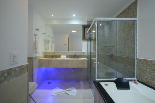 Faro Hotel Atibaia في أتيبايا: حمام مع حوض استحمام ودش مع إضاءة أرجوانية