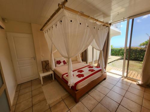 een slaapkamer met een hemelbed en een raam bij AU SOLEIL COUCHANT in Punaauia