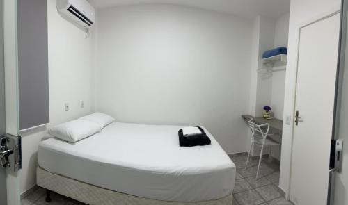 a white bedroom with a bed with a black bag on it at Apartamento em Uberlândia - Apê do Pedro in Uberlândia