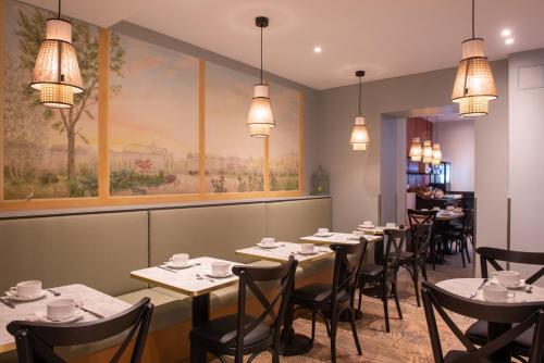 a dining room with tables and chairs and a painting at Au Pacific Hotel in Paris