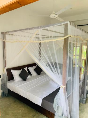 a bedroom with a canopy bed with white sheets and pillows at Pearl Gardens Midigama in Midigama