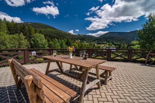 a wooden table and benches on a patio with mountains at MINERVA in Špindlerův Mlýn