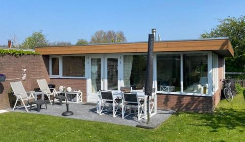 a patio with chairs and tables in a yard at Vakantiebungalow in Riviera Maison stijl nabij zee en strand, bos en duin in Warmenhuizen