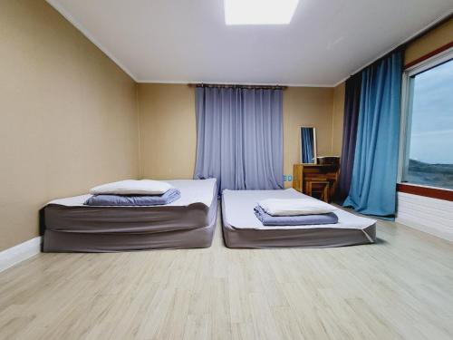 two beds in a room with blue curtains at Morning Beach Pension in Jeju