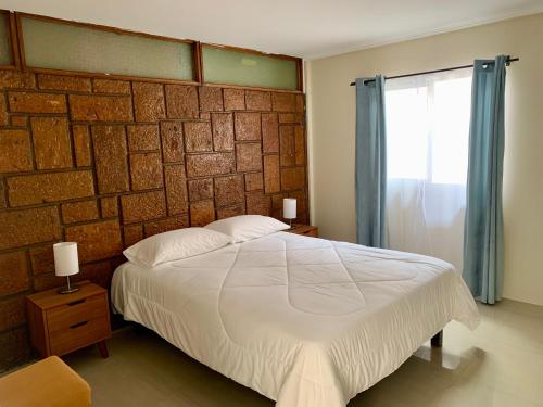 a bedroom with a white bed and a brick wall at Península Hostel & Coffee in Iquique