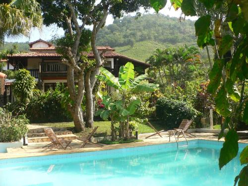 una piscina con 2 sillas y una casa en Hotel Eco Sítio Nosso Paraíso, en Saquarema