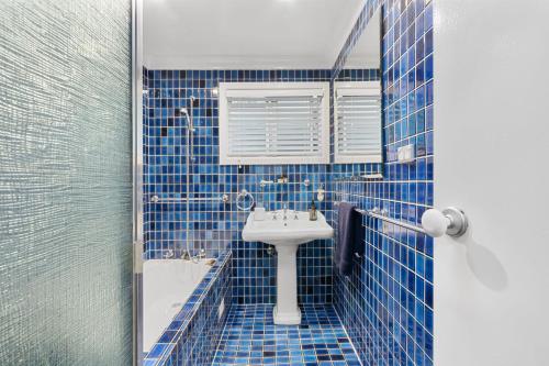 a blue tiled bathroom with a sink and a mirror at Pearl House By Coast Holidays in Pearl Beach
