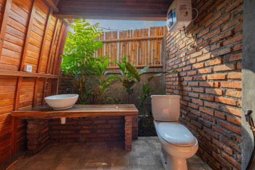 a bathroom with a toilet and a brick wall at Kubu Selat Villa and Glamping in Gianyar