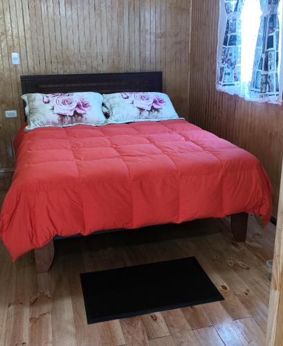 1 cama con edredón rojo y 2 almohadas en Cabaña Los Pajaritos dos de Frutillar en Frutillar