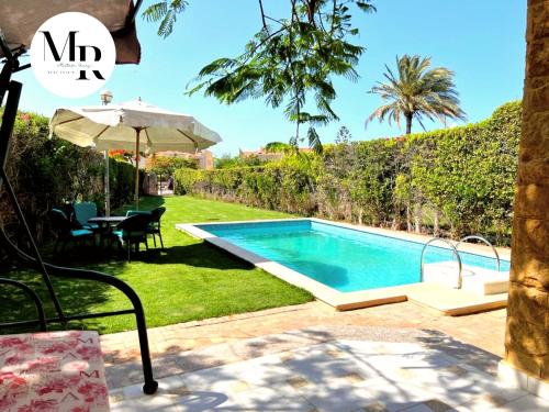 einen Pool im Garten mit einem Tisch und einem Sonnenschirm in der Unterkunft Villa Marina (5) 2nd Row Of The Sea in El-Alamein