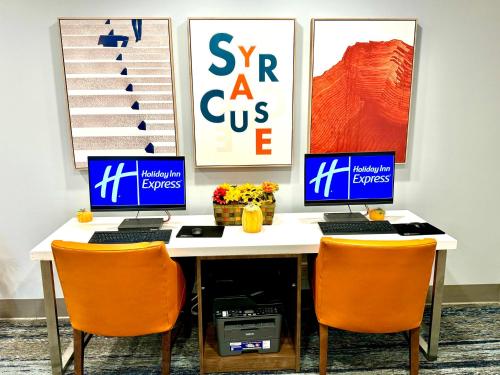 a desk with two computers on it with orange chairs at Holiday Inn Express & Suites Dewitt - Syracuse by IHG in East Syracuse