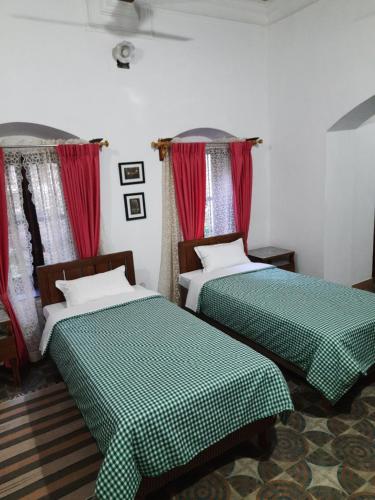 two beds in a room with red curtains at Heritage Home, Hampe's in Mysore