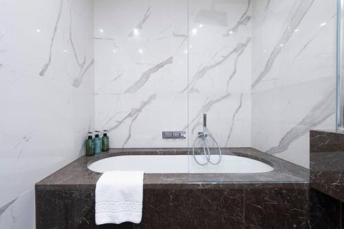 a bathroom with a bath tub with a marble wall at Garden Haven: Luxe 1BR 1BA Chigwell Retreat in Chigwell
