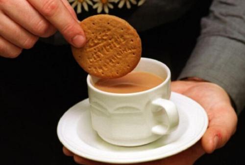 Eine Person hält einen Keks neben einer Tasse Kaffee. in der Unterkunft Shinjini Resort in Mandarmani