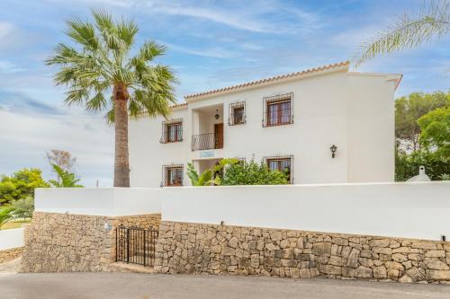 a white house with a stone wall and a palm tree at La Boniquesa in Benissa