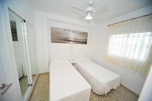 Cette chambre blanche comprend deux lits et un ventilateur de plafond. dans l'établissement Estoril III vista mar Orangecosta, à Benicàssim