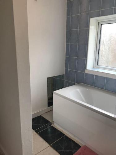 a bathroom with a white tub and a window at Lovely 1 bed flat in great location with garden in Ilford