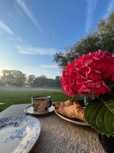 un tavolo con piatti e un vaso con una rosa di Le Manoir de la campagne a Yébleron